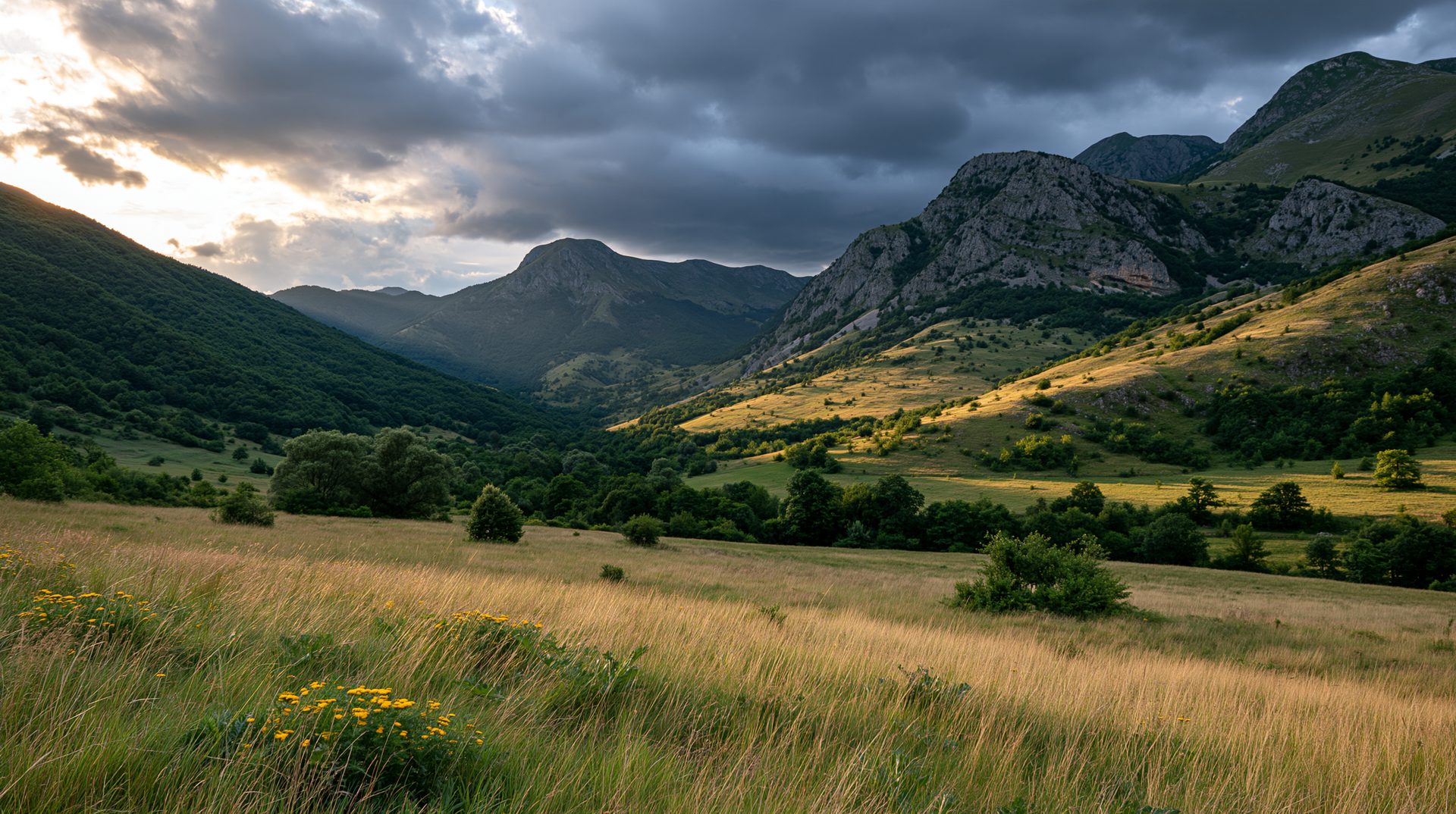 A dramatic wide-angle landscape photograph of a green mountain valley in Bosnia under heavy storm clouds, with a patch of afternoon sunlight brightly illuminating the rocky hillsides and a grassy field in the foreground.